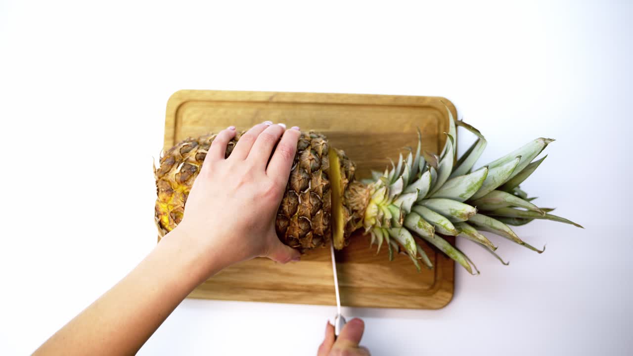Pineapple against white background. Slicing ripe pineapple with sharp knife on table