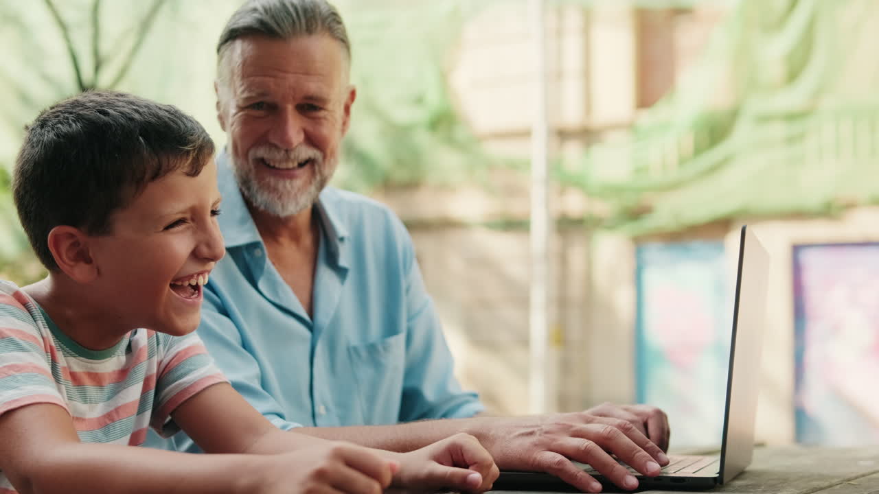 Grandfather and Grandson Laughing While Using Laptop Outdoors