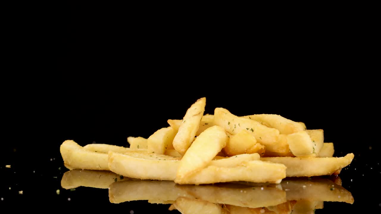 Golden French fries rotate smoothly on a reflective black surface, illuminated by studio lighting. The camera maintains a steady, centered perspective throughout the 11-second video