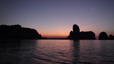 barco de motor en el agua cristalina durante un amanecer naranja en krabi tailandia con siluetas de montaña de piedra caliza en la distancia