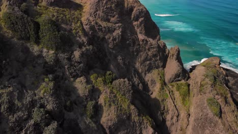 hombre controlando un avión no tripulado de pie en un acantilado rocoso cerca de la playa de te werahi durante el día en cape reinga, isla del norte, nueva zelanda