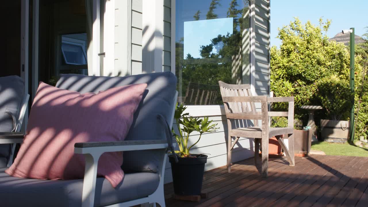 Pink pillowed armchair is sitting still on deck while camera is panning right, revealing garden