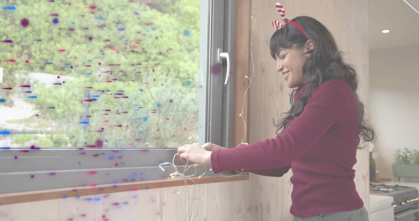 Woman grabbing lights coil at countertop then wrapping strand along window frame for home decor
