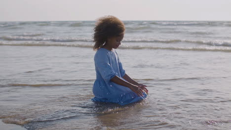 cute girl in blue dress sitting kneeling on the seashore