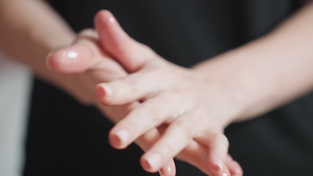 Close-up of light skin woman gently rubbing cream between her palms with focus on moisturized hands and blurred black clothing in background, emphasizing personal care, and hygiene in daily routine