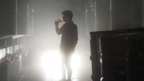 a guy drinking beer from a tank in brewery in glass with a contrast light behind him