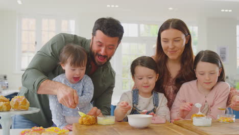 family with down syndrome daughter baking and decorating cakes sitting around table at home