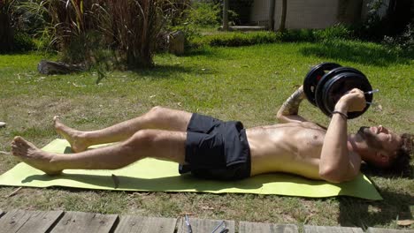 working out outdoors, a man does dumbbell presses on his lawn in the sun