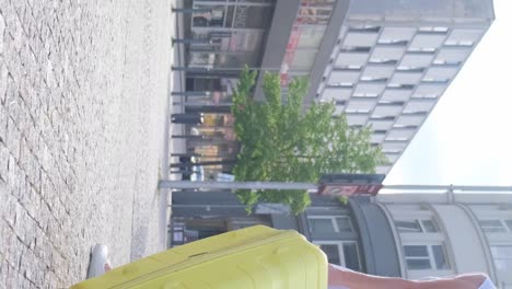 slow motion of a female tourist in a fashionable outfit walking down a european street and carrying her bright yellow wheeled suitcase. vacation and travel