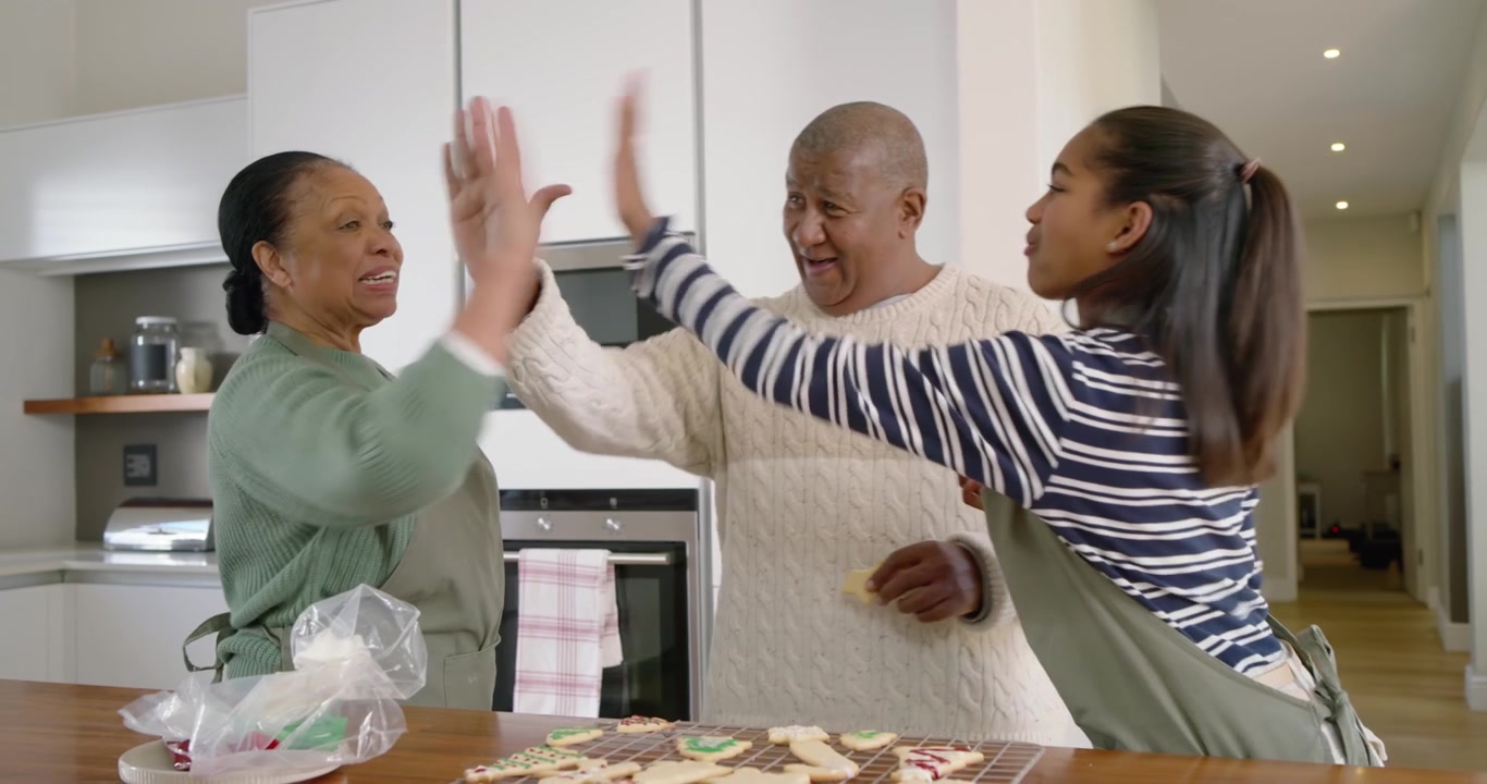 Famiglia afroamericana in cucina, ragazza adolescente che sprema una sac à poche di glassa su una griglia di raffreddamento assaggiando i biscotti.