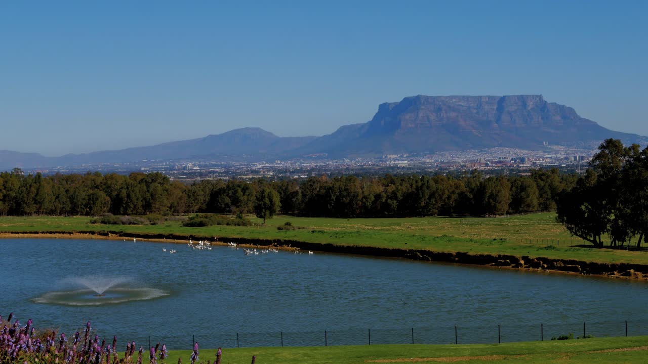 Distant view of majestic Table Mountain and Cape Town, with a dam and fountain spraying water in the foreground