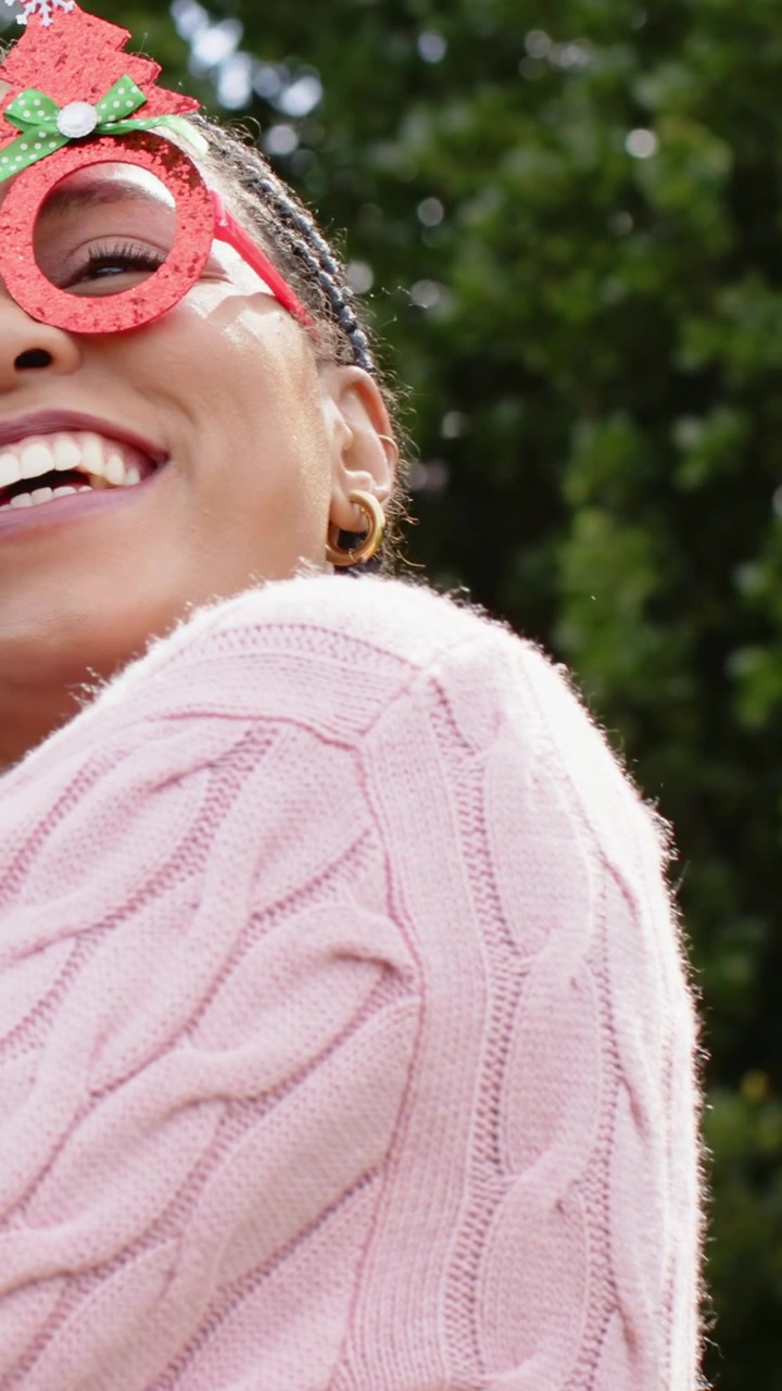 Video verticale: Panoramica su una donna che si gira e ride verso la telecamera al parco, con maglione rosa e occhiali da sole rossi.