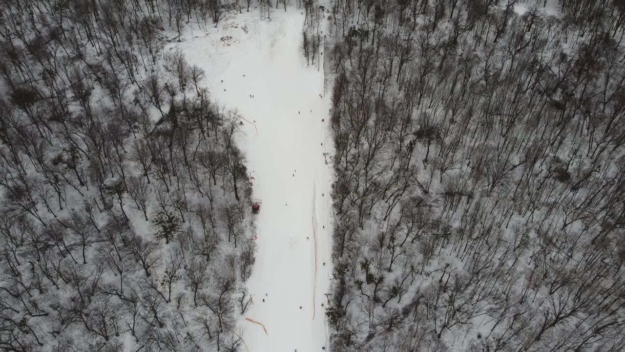 Skiers and snowboarders skiing on snow slopes with ski lift at weekend. Drone flying over snowy Slope with Skiers and Snowboarders at Ski Resort on a frosty winter day: drone view