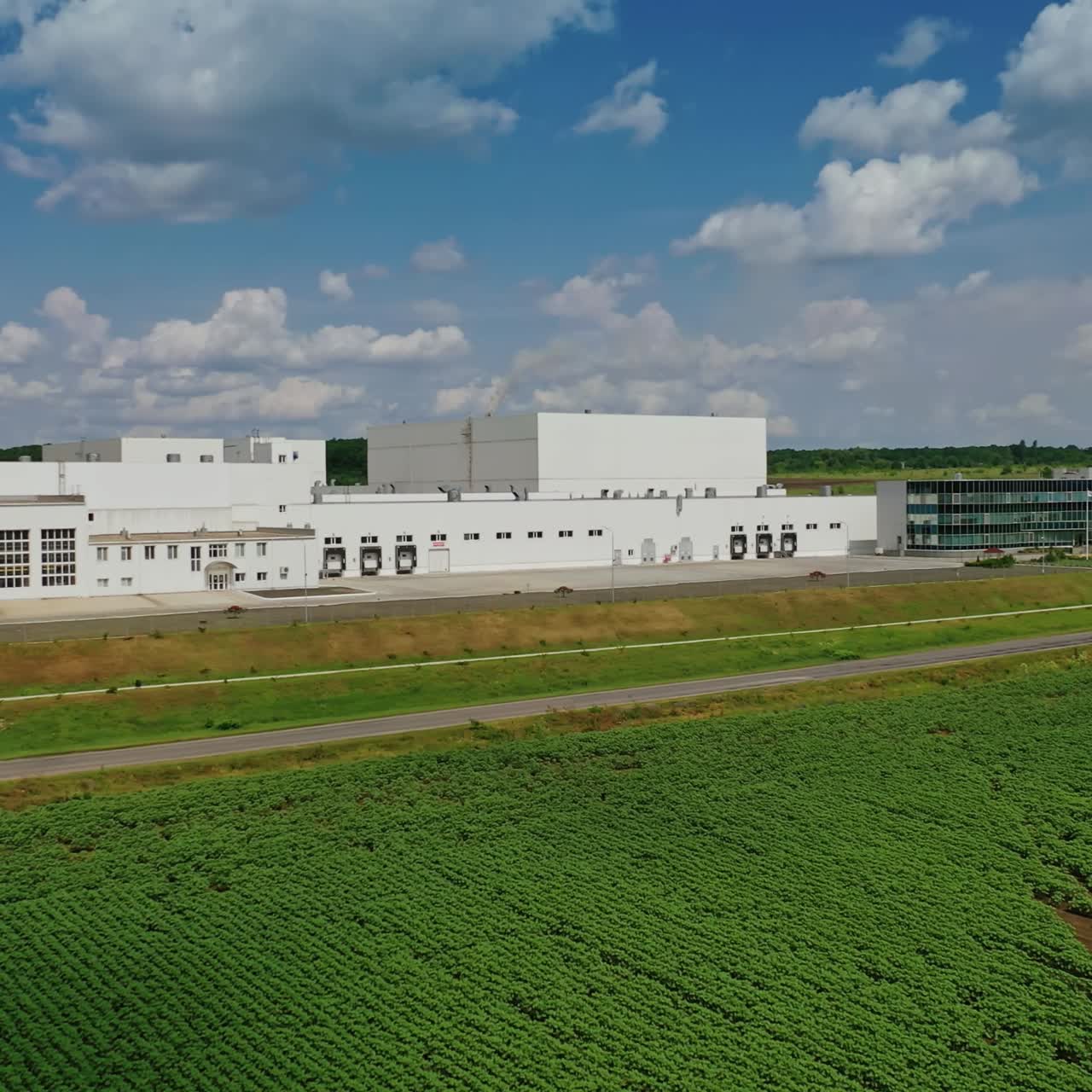 White manufacture on field. Large industrial territory among nature under the blue sky. Exterior of modern factory in the countryside. Front view.