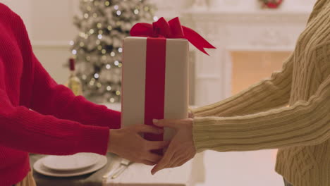 unrecognizable woman giving a gift box to her friend during christmas dinner at home