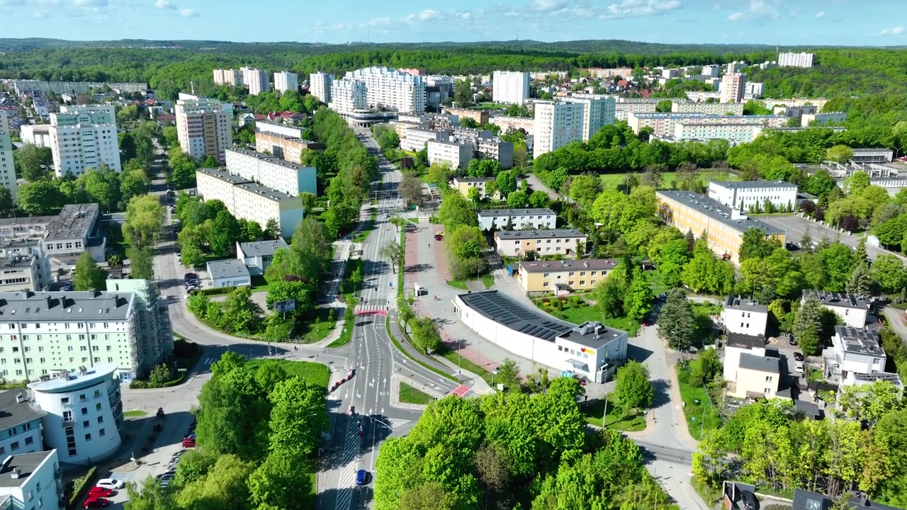 Elokuvamainen ilmakuva Gdynian kaupunginosasta, jossa näkyy reheviä vihreitä puita, asuinrakennuksia ja kaupunki-infrastruktuuria kirkkaassa päivänvalossa.