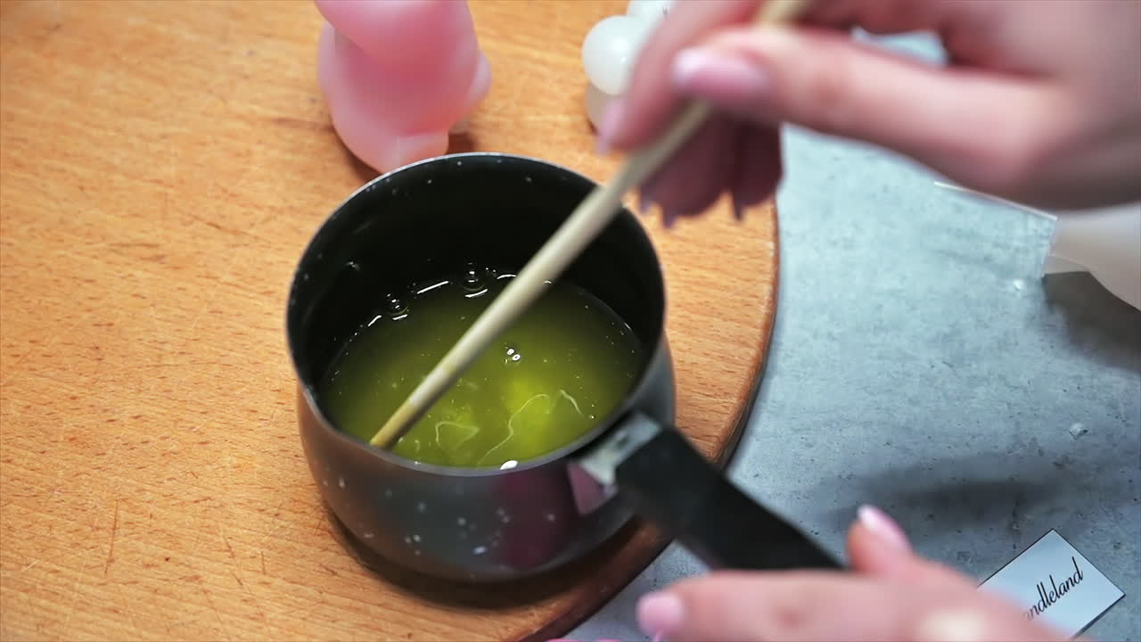Hand made candles production, female hand mixing melting wax in a pot. Slow motion