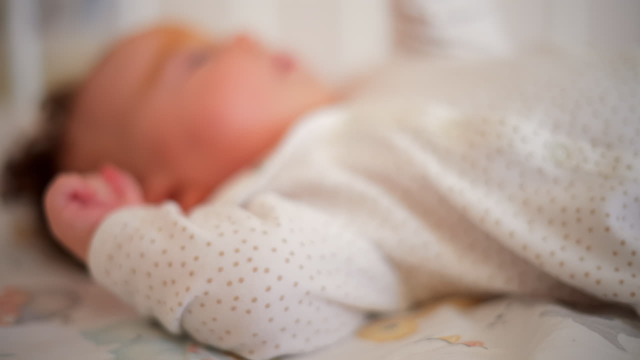 Un neonato in vestiti morbidi si muove delicatamente in una culla, allungando le piccole mani nella luce naturale del mattino