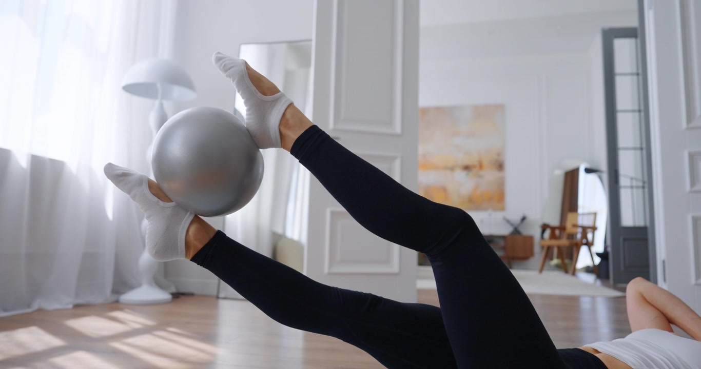 Young Woman Doing Pilates Core Exercise with Small Ball at Home