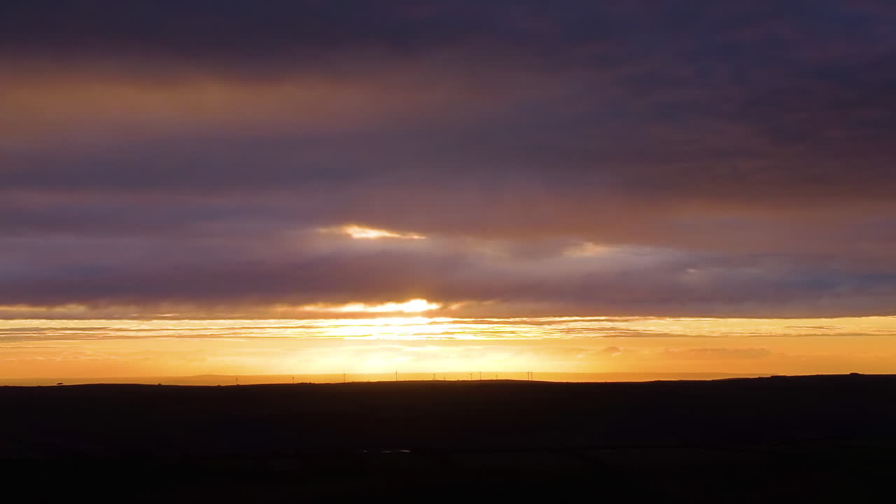 Langsomt luftpanorama hen over solnedgangslandskab med land nedenfor i dyb, mørk skygge, mens solen dykker ned under horisonten. Ideel til meditationsvideoer, wellness branding og afslappende naturindhold