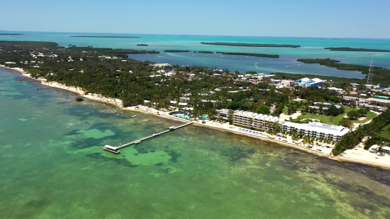 Turquoise waters meet white beach in aerial flyover of lush Cheeca Lodge coast, aerial panoramic establishing