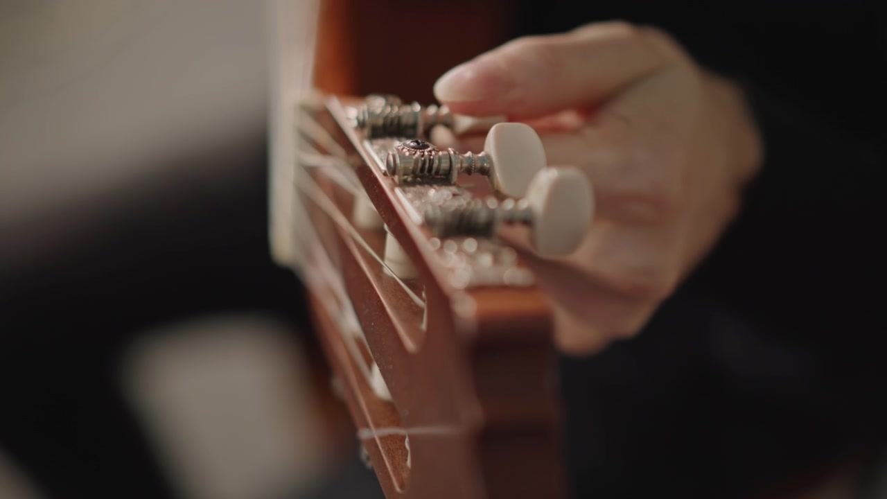 Hands adjust tuning pegs carefully. Focus on precise adjustment of guitar tuning pegs during practice. Calmly tuning guitar strings with careful attention to hardware for optimal sound quality