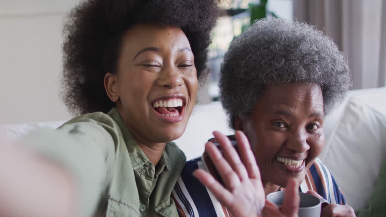 Happy african american adult daughter and senior mother taking selfies, slow motion