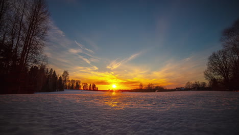 Snowy,-winter-landscape-timelapse-and-the-orange-sun-on-the-horizon,-with-the-clouds-advancing