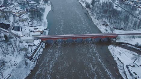 vista aérea de los rápidos del río venta durante la inundación de invierno, viejo puente de ladrillo rojo, kuldiga, letonia, día de invierno nublado, amplia toma de drone moviéndose hacia adelante inclinándose hacia abajo