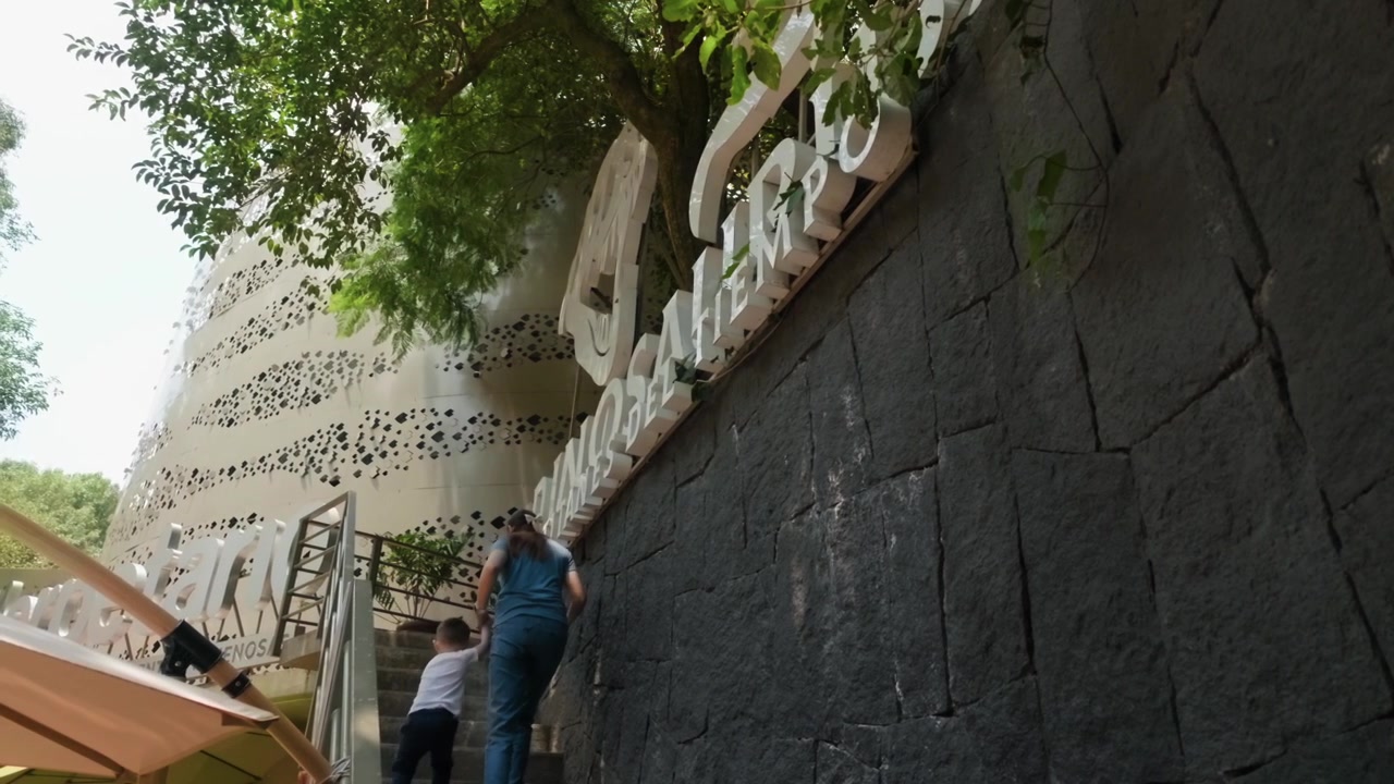 Una madre e suo figlio salgono le scale verso la mostra dei dinosauri allo Zoo di Chapultepec a Città del Messico. Il bambino cammina davanti alla madre, entrambi esplorando l'attrazione pubblica.