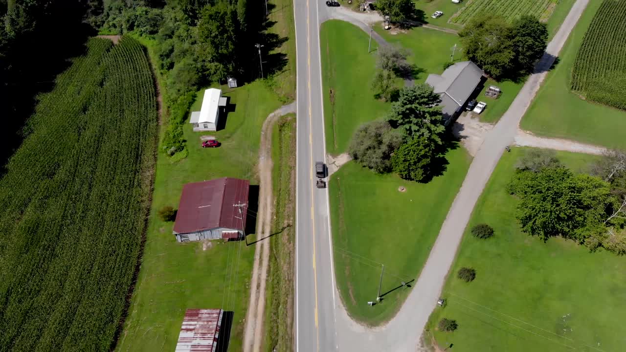 햇살 좋은 날 옥수수밭과 나무 주변으로 출퇴근하는 자동차가 있는 시골길의 공중 전망