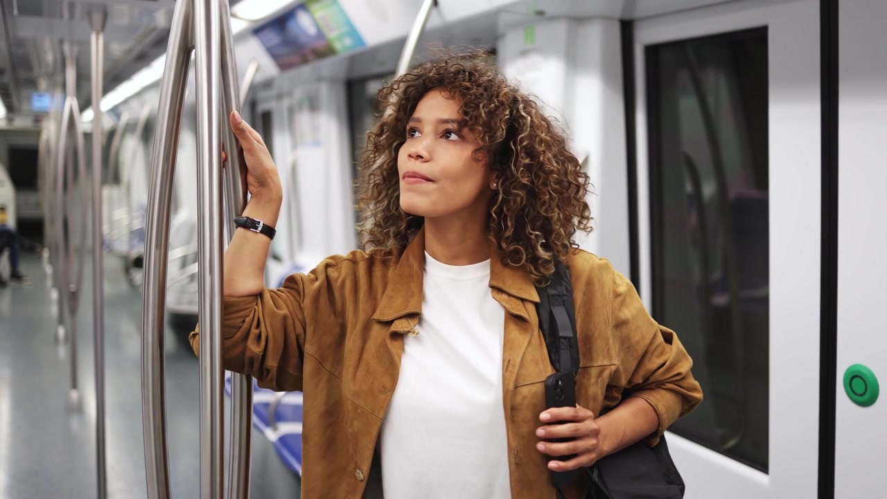 Giovane donna con capelli ricci che fa il pendolare su un treno della metropolitana