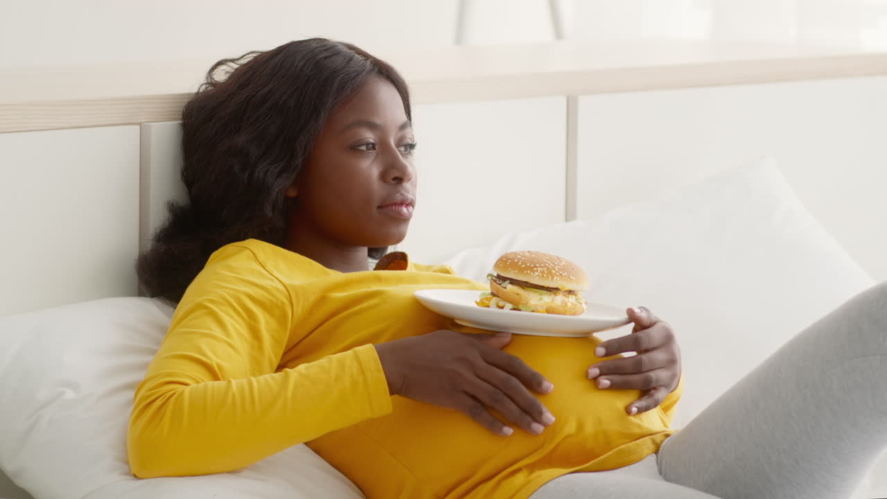 Donna incinta che mangia un hamburger a letto