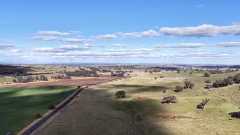 aerial drone footage glides over open farmland and a rural road under bright daylight, revealing fields, scattered trees, and expansive blue sky