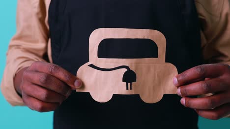hombre de raza mixta sosteniendo un coche de papel con enchufe de recarga en fondo azul del estudio concepto de coche eléctrico ecológico