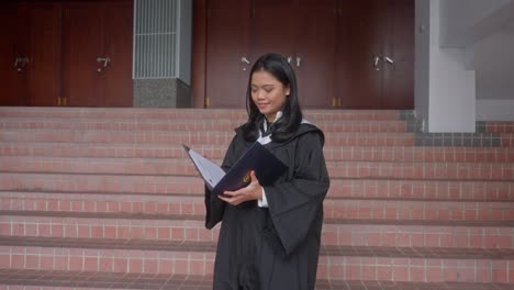 asian indonesian girl wearing graduation gown opening folder with certificate proudly