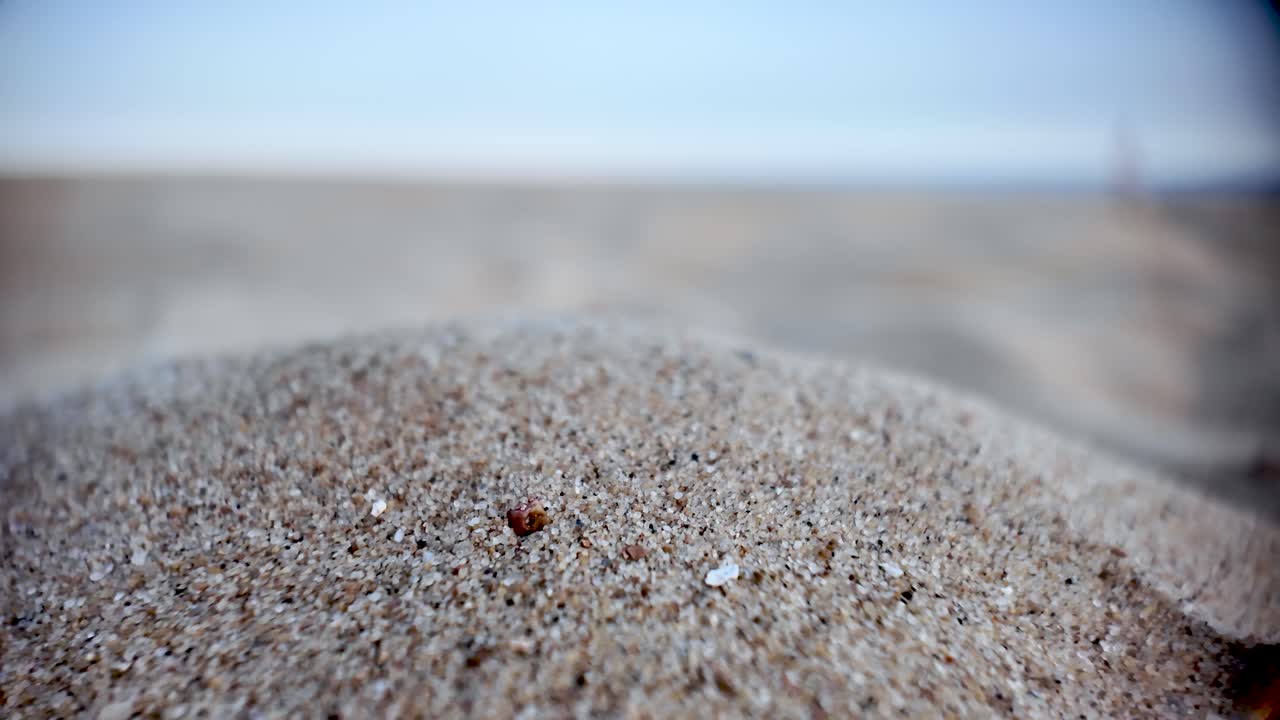 Close up view of sand grains with blurred beach and sky in background. macro shot, dolly right