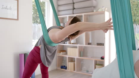 focused diverse fitness teenage girls in aerial yoga class in big white room, slow motion