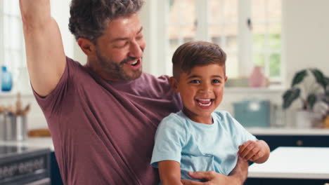 Mature-Father-At-Home-In-Kitchen-With-Son-Celebrating-After-Finishing-Jigsaw-Puzzle-Together