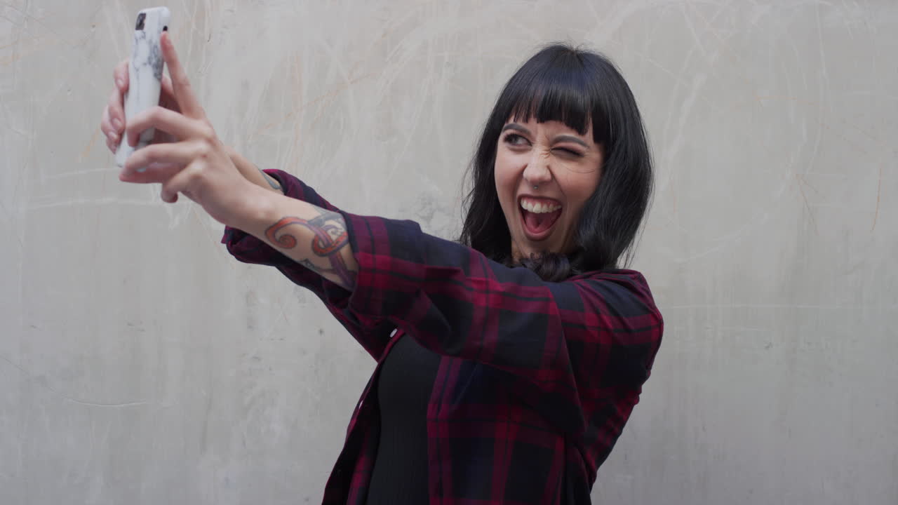 ritratto di una giovane donna tatuata che usa uno smartphone che posa prendendo un selfie facendo facce godendo della tecnologia dei telefoni cellulari condividendo la connessione