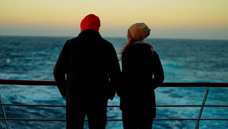 fun couple in warm coats and red beanie hats standing at sunset in the antarctic peninsula