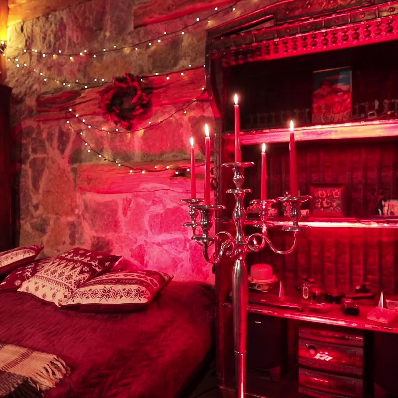 Cozy bedroom made in medieval style with Christmas decorations. Big bed among two pieces of furniture and long candlesticks lit in red light