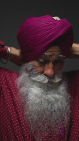 vertical video low key studio lighting shot of senior sikh man with beard tying fabric for turban against dark background 1