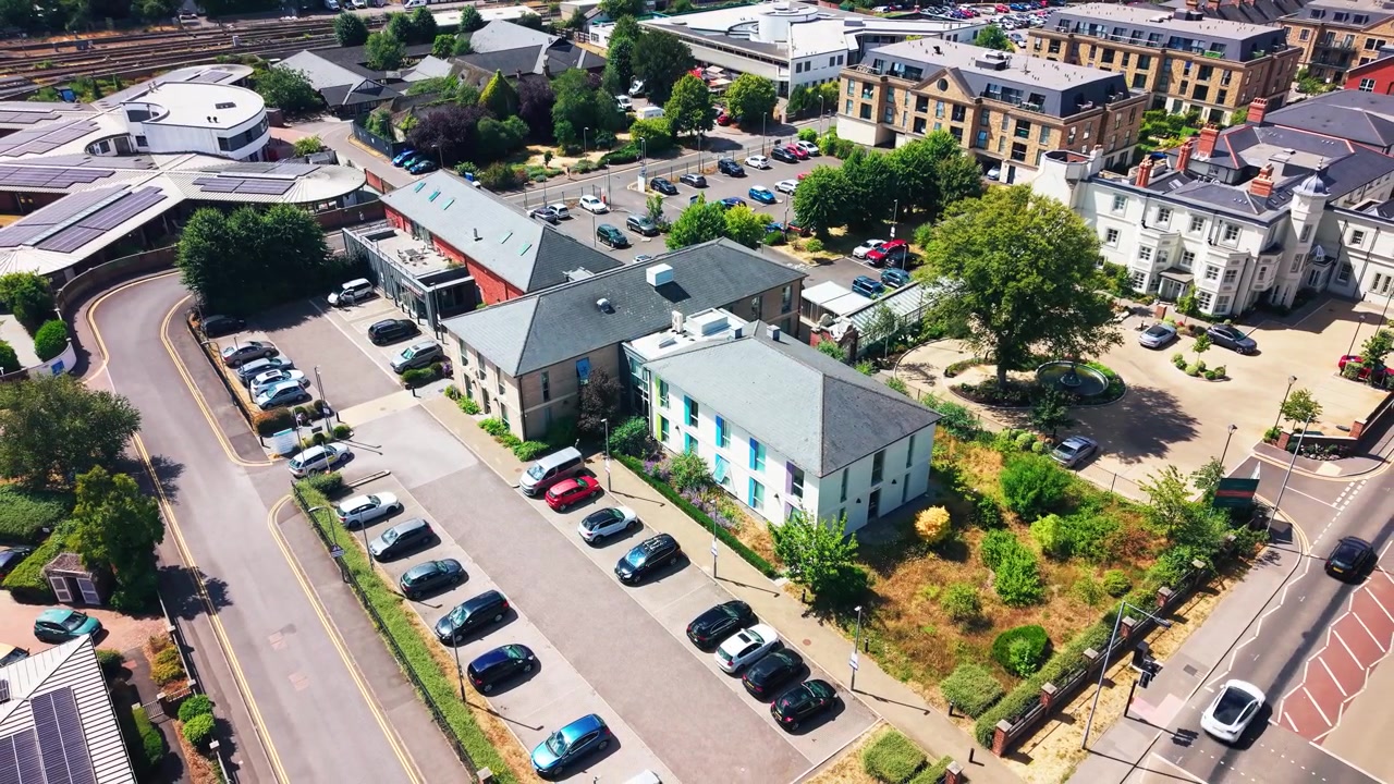 Riprese aeree con drone che sorvolano un moderno edificio sanitario dell'NHS con persiane colorate, parcheggi e giardini circostanti in una città inglese.