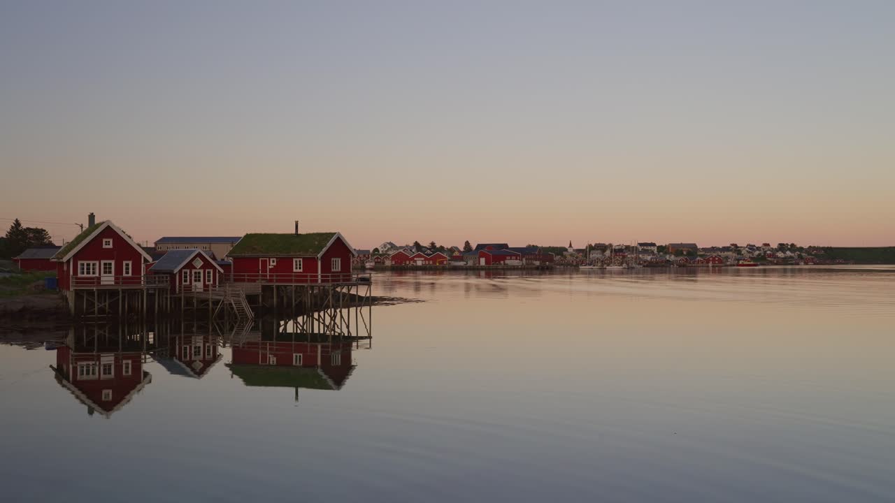 aldea de lofoten con casas rojas que se reflejan en el agua tranquila al amanecer en reine, noruega
