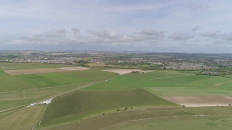 Aerial-tracking-north-from-Maiden-Castle,-the-towns-of-Dorchester-and-Poundbury-is-visible-in-the-background