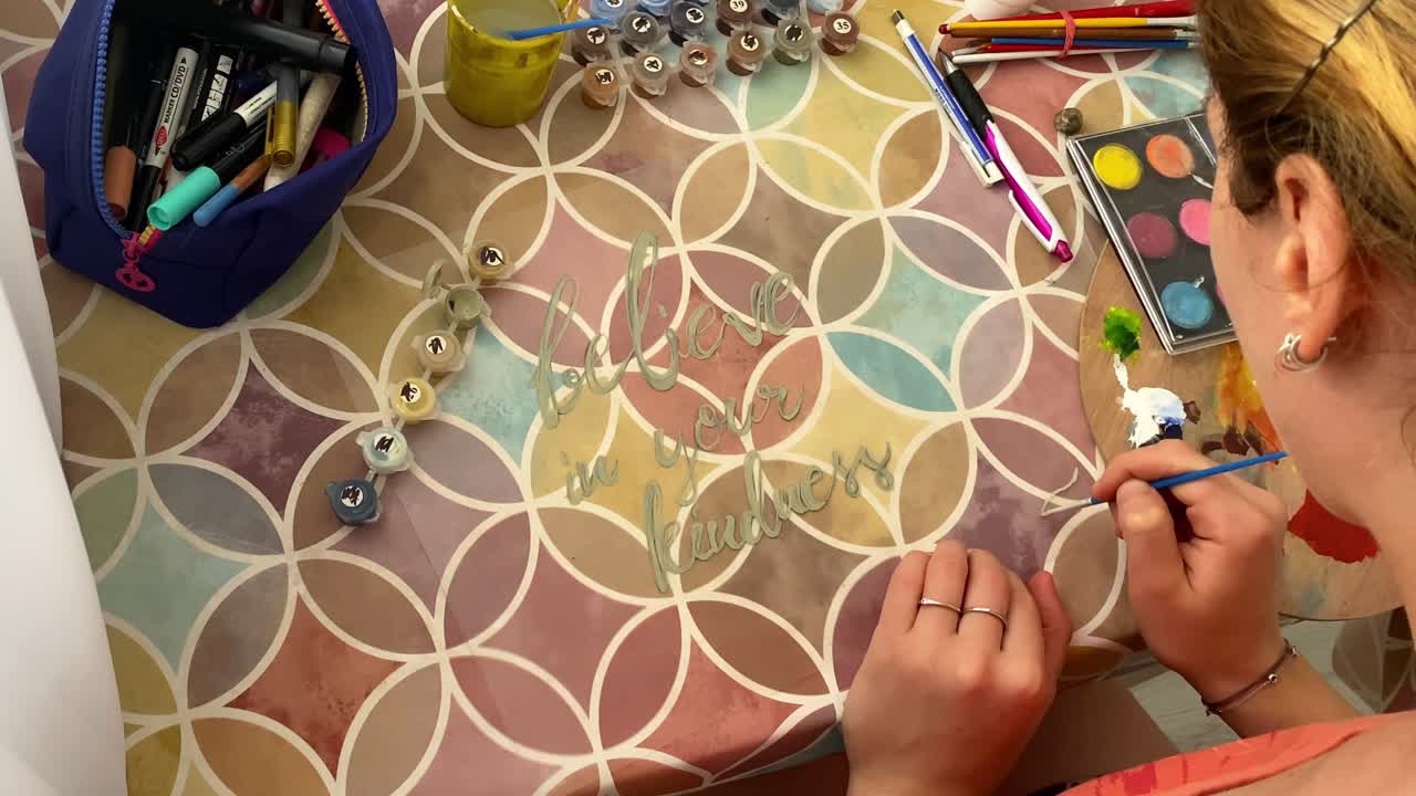 disparo de arriba hacia abajo sobre una joven artista femenina pintando una imagen en lienzo con pincel y colores de tempera de agua