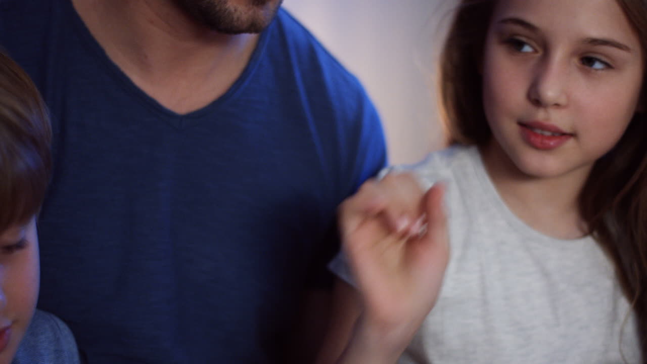 밤에 두 아이가 침대에 앉아 이야기하고 무언가를 보는 백인 아버지의 클로즈업 보기