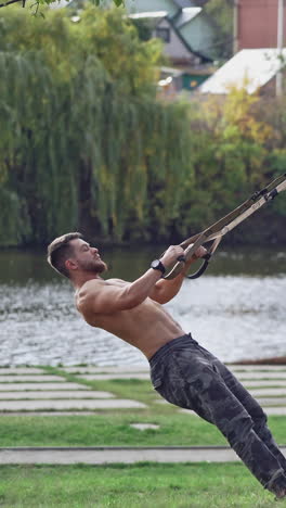 training in open air. young man working out by the lake in city park. vertical video