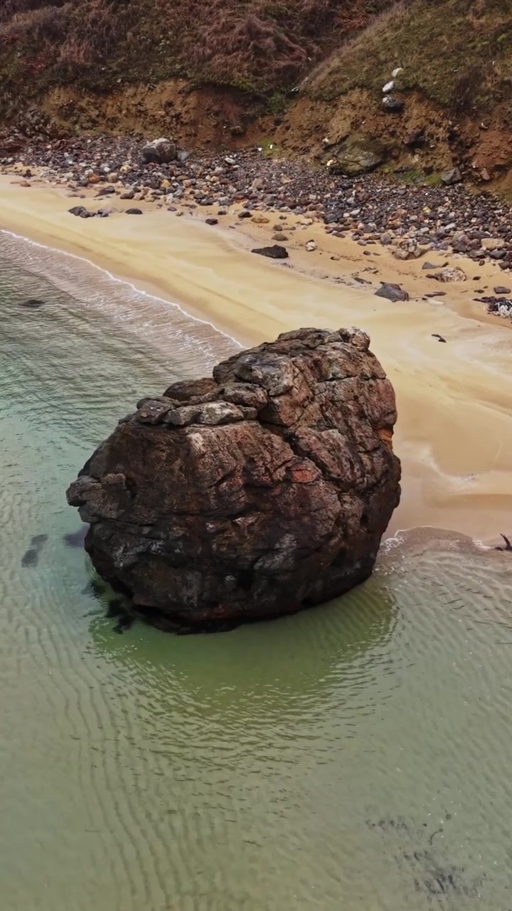 Grande roccia su una spiaggia sabbiosa vicino ad acque calme sotto un cielo nuvoloso